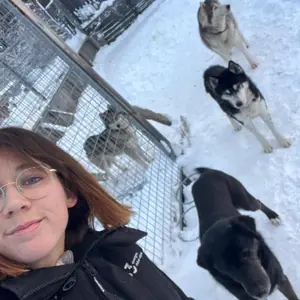 Selfie de Juliette dans un enclos enneigé, entourée de plusieurs huskies