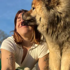 Touffe, eurasier au pelage roux, faisant un bisou à Juliette sous un ciel bleu
