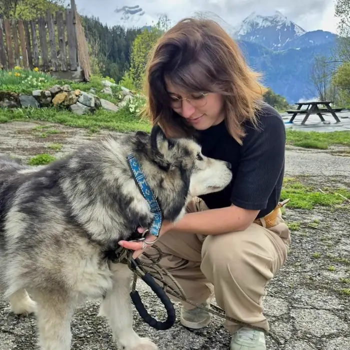 Femme accroupie auprès d'un husky en laisse, devant un paysage de montagne